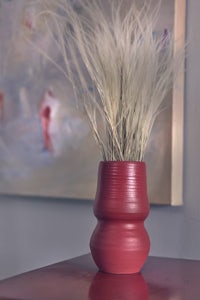 a red vase on a table next to a painting